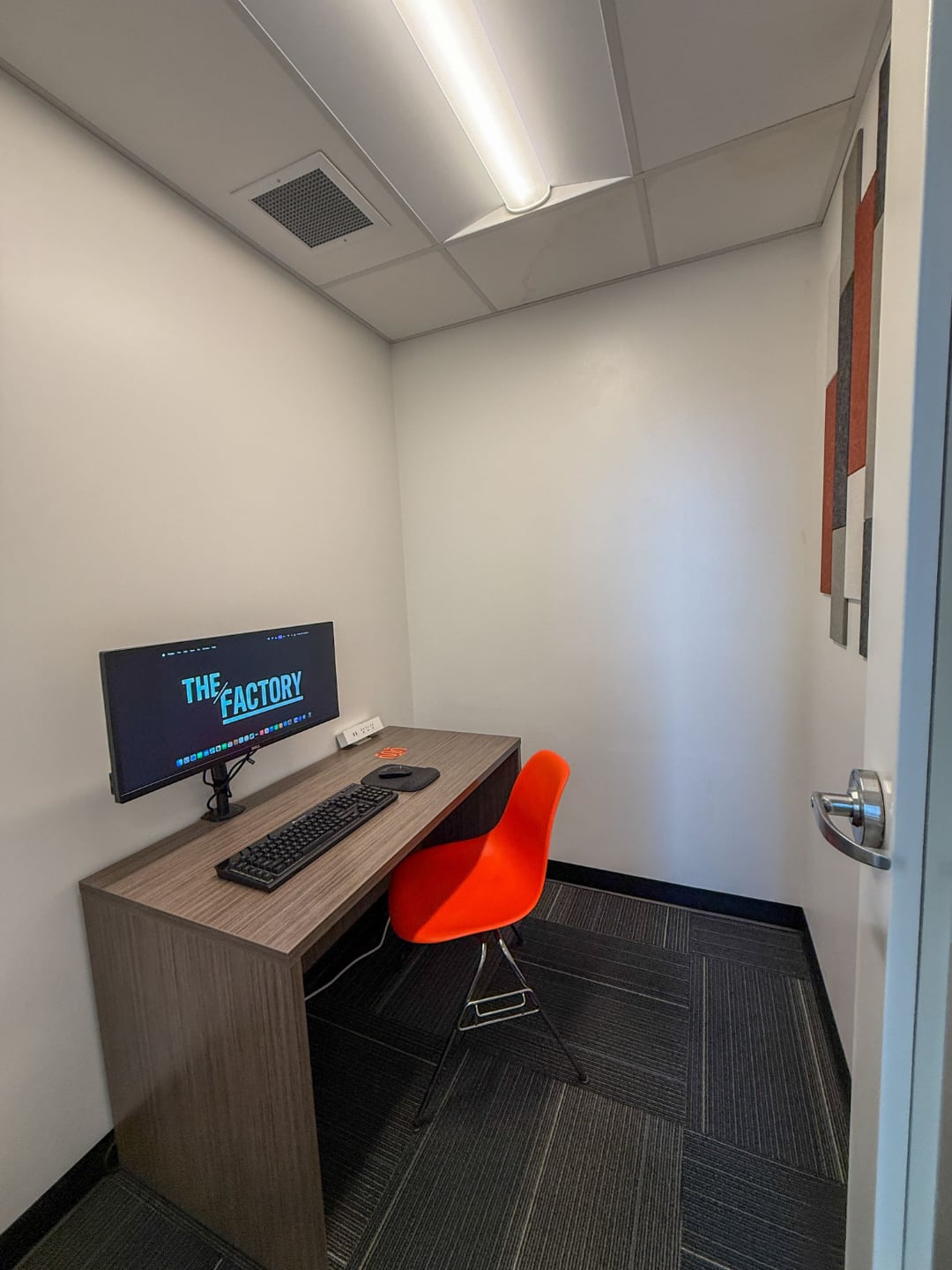 Photo of The Factory video call booth with an orange plastic chair and an a wooden desk placed on the west side of the room
