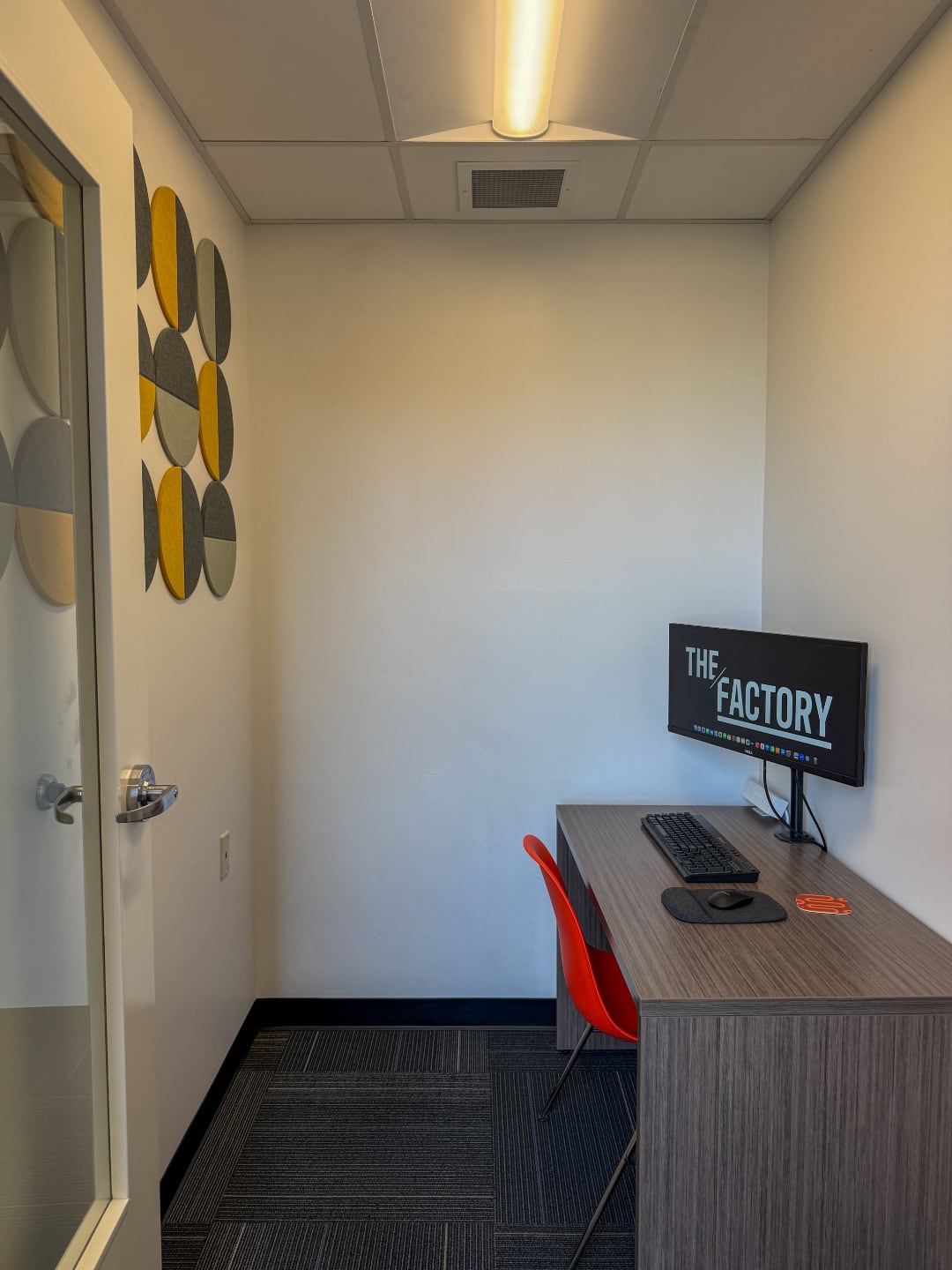 Photo of The Factory video call booth with an orange plastic chair and an a wooden desk placed on the east side of the room
